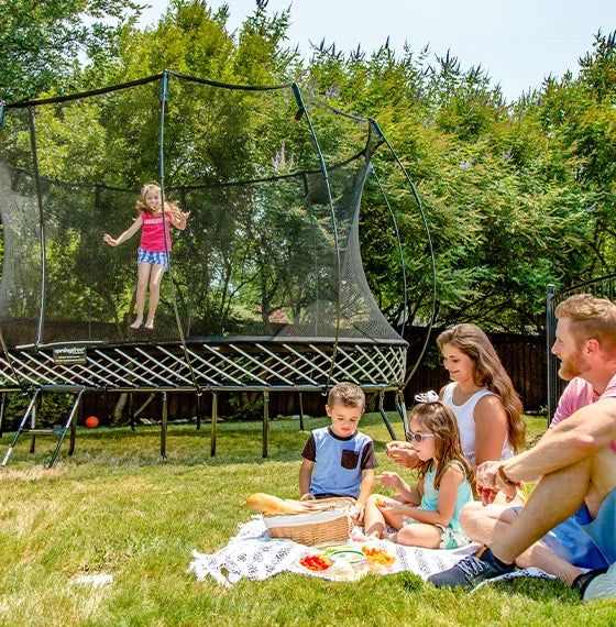 a kid playing on a trampoline and a family having a picnic outside