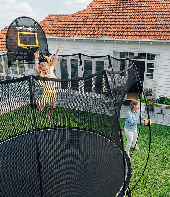 A kid jumping on a trampoline, a woman playing with a ball outside