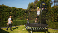 Charger l'image dans la visionneuse de galerie, A boy on a trampoline shooting a ball in a hoop, a man holding another ball at the backyard