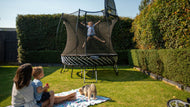 Charger l'image dans la visionneuse de galerie, Kid playing on a trampoline, a woman and a boy sitting and watching her. A dog with them
