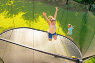 Charger l'image dans la visionneuse de galerie, A girl jumping on a trampoline and another girl running around