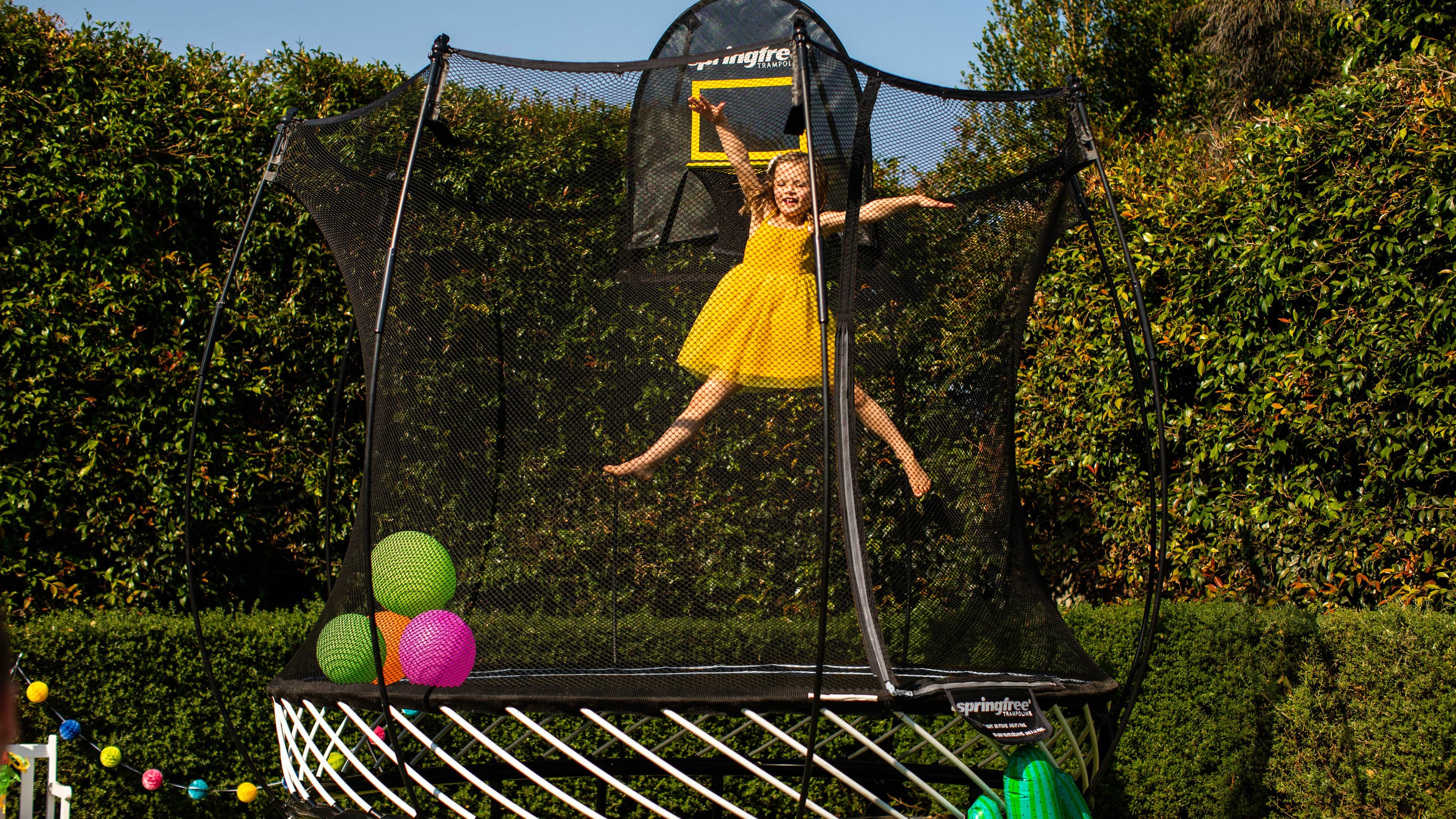 A gril in yellow dress playing on a trampoline with balloons in it